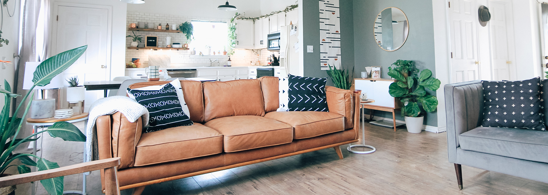 Woonkamer met bruine bank en witte keuken op de achtergrond